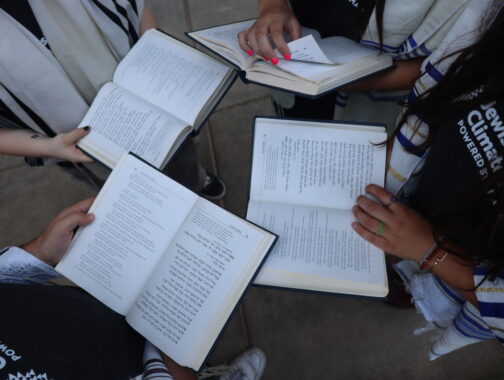 Jewish Youth Climate Movement teens holding siddurim (prayer books) and wearing tallit (prayer shawls) while standing in a circle.