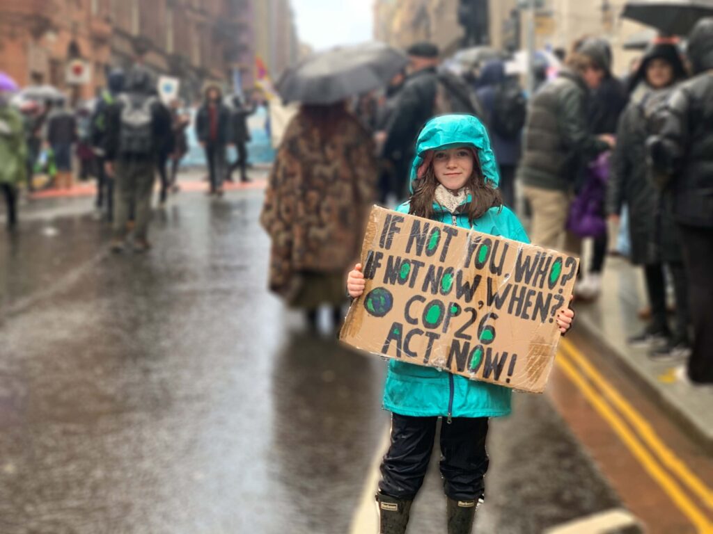 Girl holding cardboard sign that says "If not you, who. If not now, when."