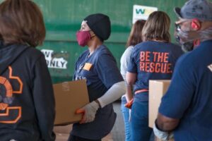 Volunteers wearing "Be the Rescue" t-shirts, moving boxes of food.